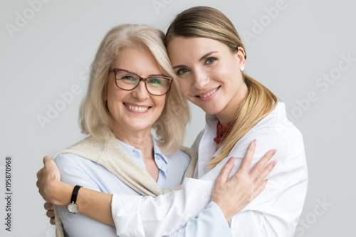 Happy beautiful older mother and adult daughter embracing looking at camera, smiling senior lady hugging young woman, family of different age generations bonding hugging, head shot portrait