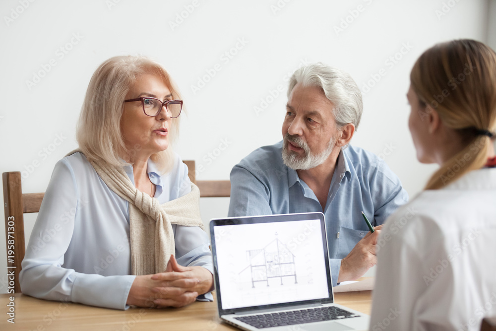 Senior couple talk to real estate agent about house purchase at meeting, interior designer advisor consulting older family with home plan on laptop screen, aged man and woman negotiating with realtor Senior couple talk to real estate agent about house purchase at meeting, interior designer advisor consulting older family with home plan on laptop screen, aged man and woman negotiating with realtor