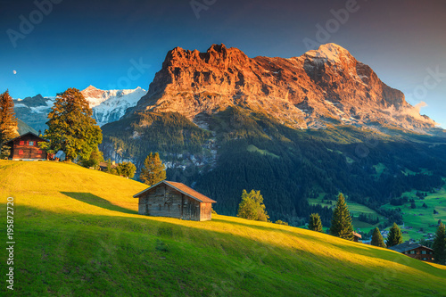 Alpine chalets with green fields and high mountains at sunset