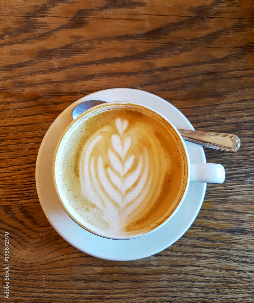 Cappuchino coffee in white porcellan cup and saucer with spoon and cinnamon close up
