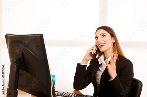 Beautiful business woman talks on smert phone in office at her desk photo