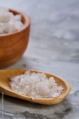 Large white sea salt in a natural wooden bowl on dark background, top view, close-up, selective focus