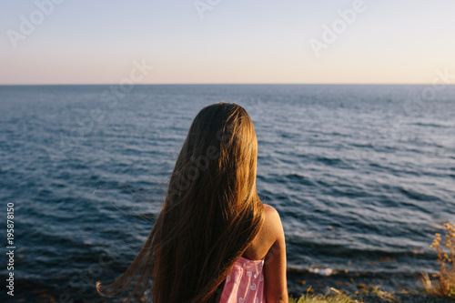 girl in a pink dress standing by the sea. rear view