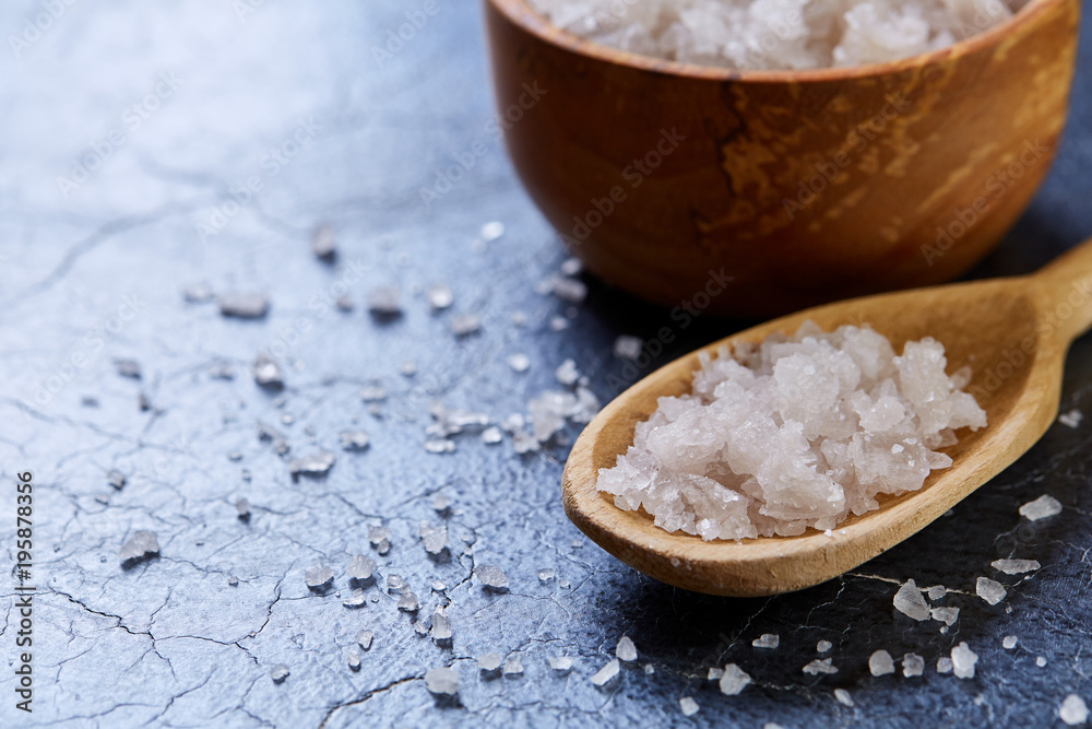 Crystal sea salt in a wooden spoon on dark background, top view, close-up, selective focus. Crystal sea salt in a wooden spoon on dark background, top view, close-up, selective focus.