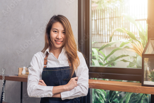 Protrait of young Asian female barista welcome her customer to coffee shop in warm light afternoon with a beautiful smile. Young female barista smile in her small coffee shop. Food and drink concept. Free Download Protrait of young Asian female barista welcome her customer to coffee shop in warm light afternoon with a beautiful smile. Young female barista smile in her small coffee shop. Food and drink concept. - GFXLoad