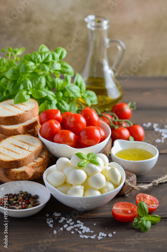 Italian food ingredients – mozzarella, tomatoes, basil and olive oil on rustic wooden table.