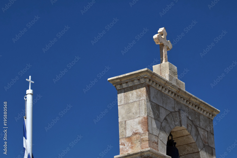 Fototapeta premium Stone Cross On The Gate and small metal cross. Stone cross on brick gate and a small metal rod with a cross on Greek flag. Greek flag is wrapped Access to the yard of the Greek Orthodox Church