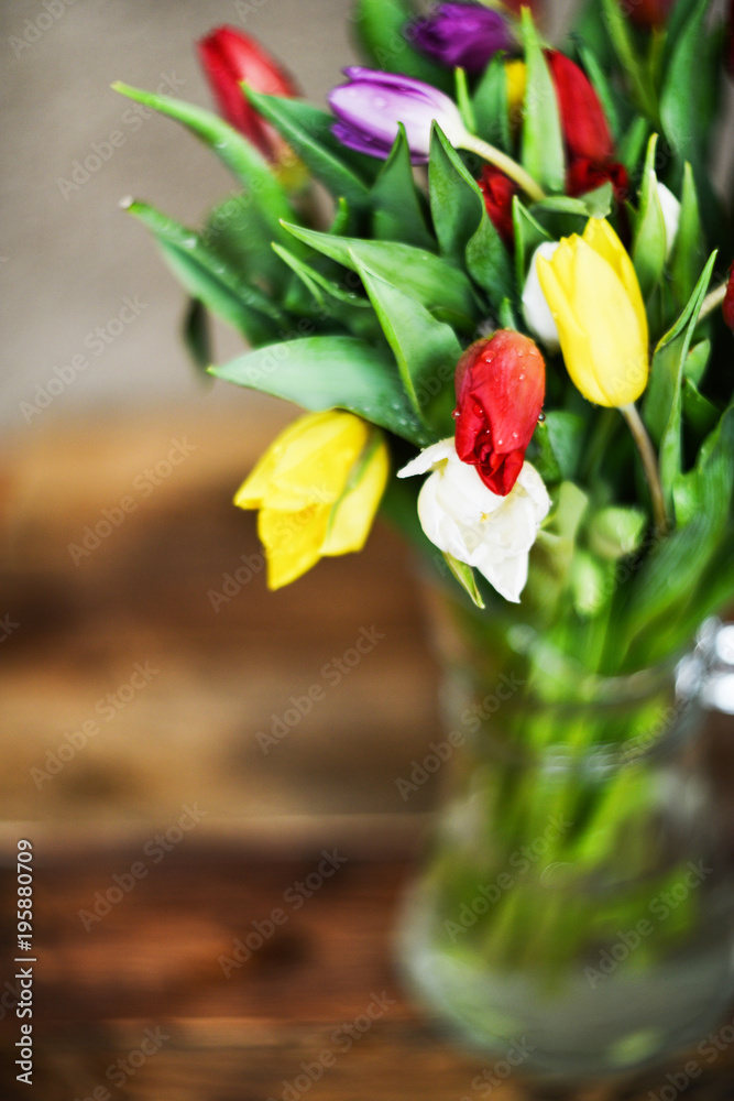 Flower background: bouquet of colorful tulips in a glass vase on a natural wooden background, postcard, mocap for mother's day greetings, international women's day