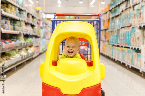 little boy happy in a supermarket cart in the shape of a car in the shopping center or mall photo