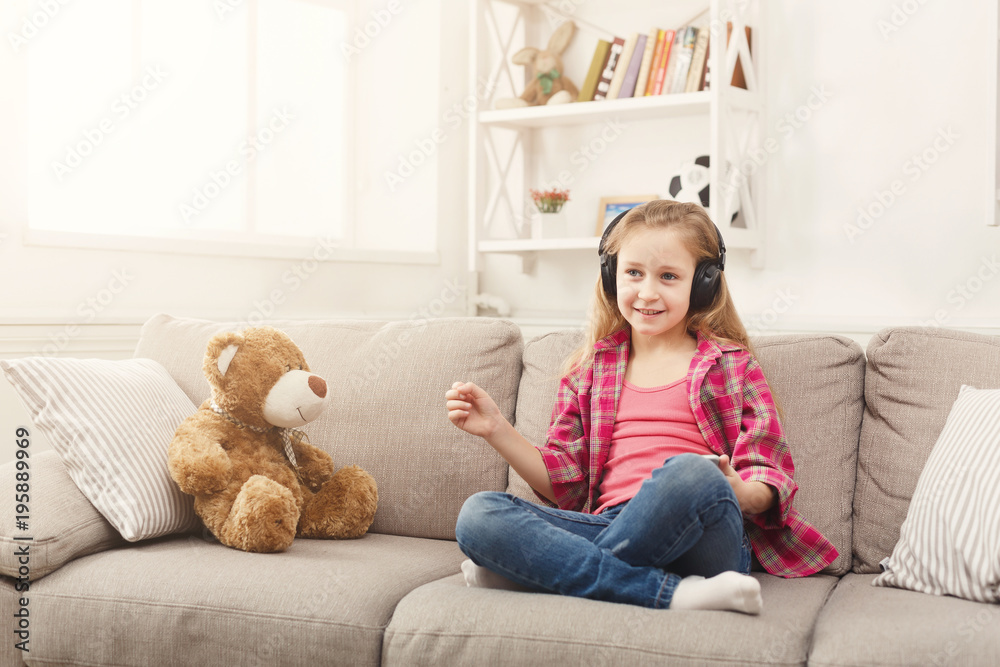 Happy little female child and her teddy bear listening to music on sofa at home Happy little female child and her teddy bear listening to music on sofa at home
