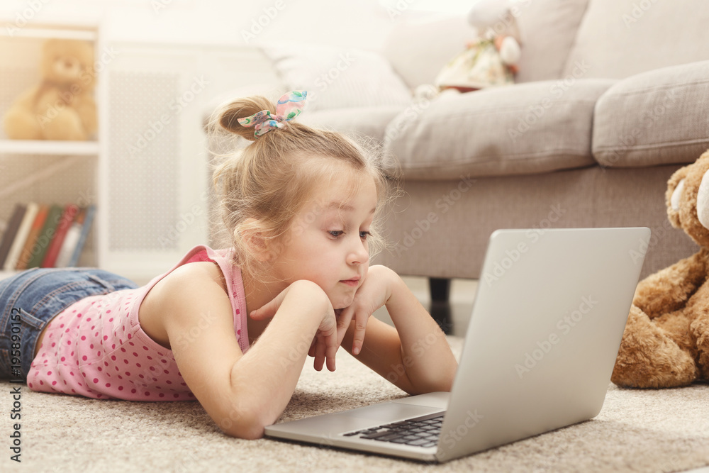 Cute little girl doing homework on laptop, sitting on the floor at home Cute little girl doing homework on laptop, sitting on the floor at home