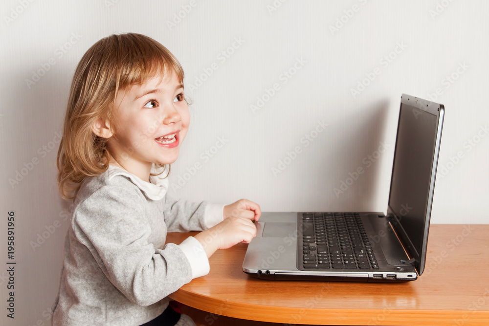Litttle baby girl sitting at the laptop on light wall background. Litttle baby girl sitting at the laptop on light wall background.