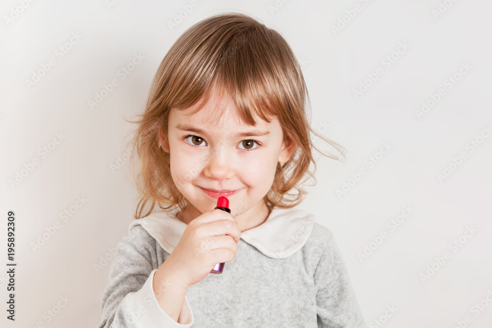 Little girl paints lips with lipstick. Light background. Little girl paints lips with lipstick. Light background.