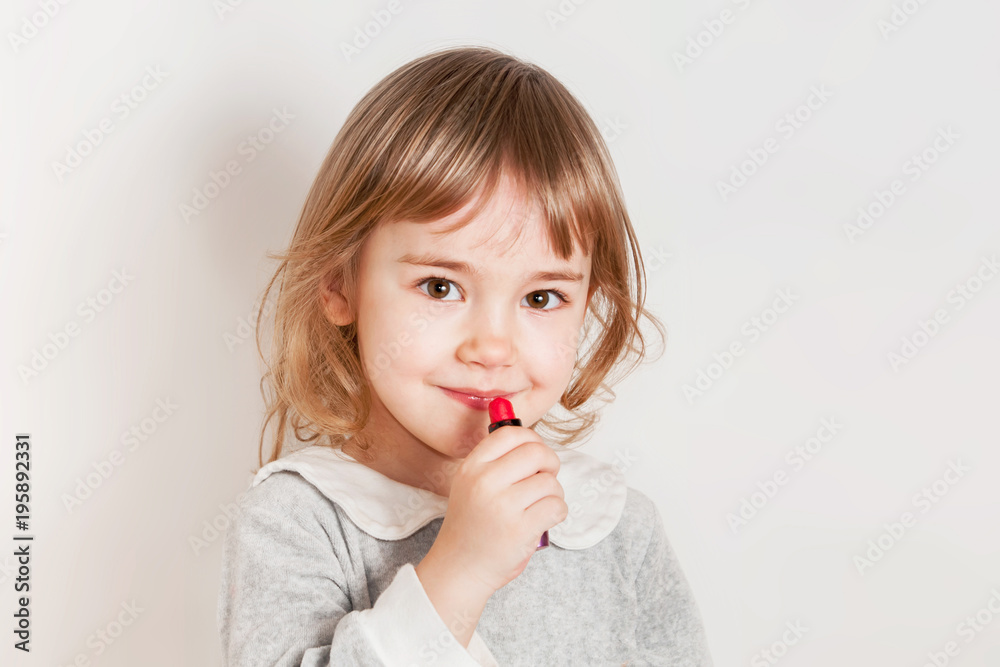 Little girl paints lips with lipstick. Light background. Little girl paints lips with lipstick. Light background.