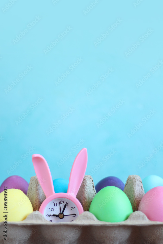 Easter raznotsvetny eggs and pink alarm clock with ears of a rabbit on a blue background