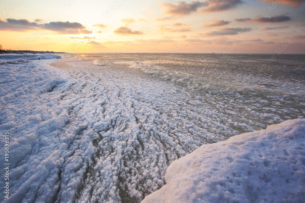 a beach under snow and a cold, ice-covered sea during sunset