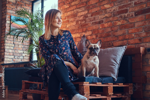 Happy woman sitting with a cute pug in a room with loft interior © Fxquadro