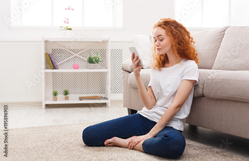 Young redhead girl with smartphone sitting on the floor