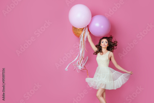 Cheerful Beautiful young girl in dress with sparkle and pink helium balloons enjoying birthday photoshoot dancing and smiling on pink background Cute woman posing in studio. Fashion Lifestyle Emotions