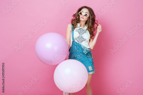 Cheerful Beautiful young girl in sunglasses with helium balloons enjoying birthday photoshoot dancing and smiling on pink background Cute woman posing in studio. Fashion Lifestyle Emotions