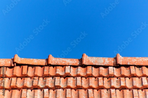 An old roof with burnt tiles. Roof in village house against a blue sky background.