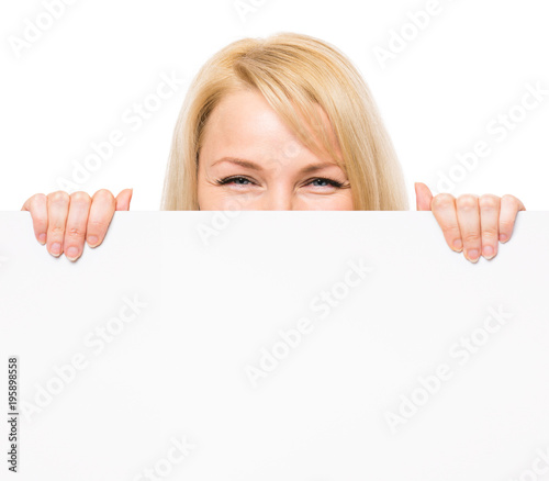 Young woman with surprised eyes peeking out from behind billboard paper poster. Businesswoman holding big white banner, isolated on white background.