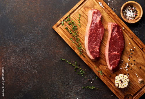Raw fresh meat Picanha steak, traditional Brazilian cut with thyme, garlic, and black pepper on wooden board. Sliced meat steaks. Copy space. Top view.