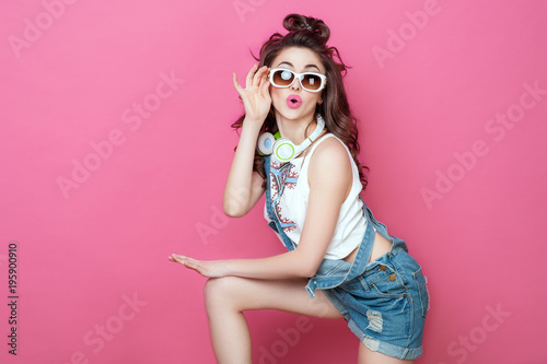 Pretty fashion cool smiling girl with headphones knitted bag sunglasses wearing a colorful clothes with curly hair dancing happy over pink background. Beauty Lifestyle Teenager People Music concept