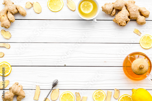 Warming tea with lemon and ginger. Cup, teapot, ginger root on white wooden background top view copy space