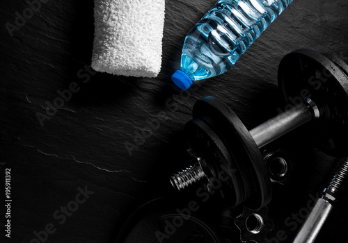 Fototapeta Naklejka Na Ścianę i Meble -  Dumbbell, bottle of water and white towel on black background. Gym accesories.