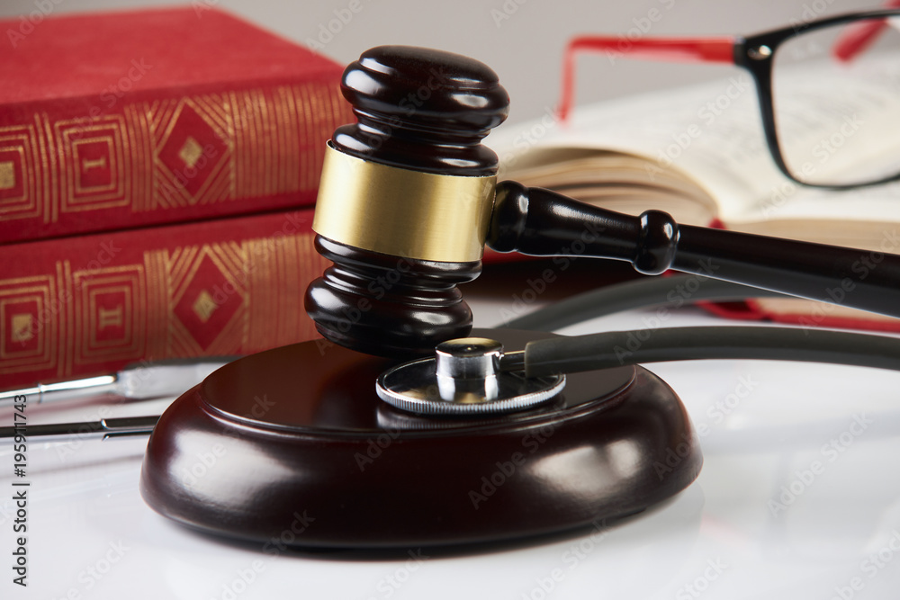 Law books with wooden judges gavel and medical stethoscope on white table in a courtroom or enforcement office, close-up. Medicine law concept. Law books with wooden judges gavel and medical stethoscope on white table in a courtroom or enforcement office, close-up. Medicine law concept.