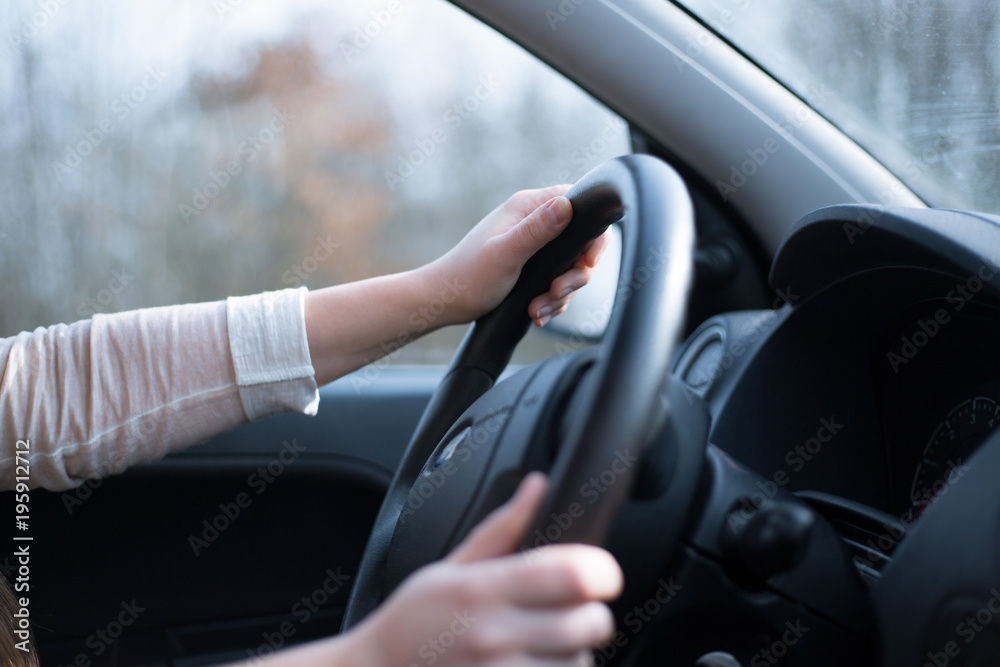 Young woman driving her new car, close-up of hands on a steering wheel