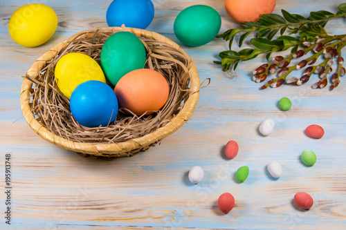 Easter eggs in a wooden basket, painted in different color on a blue background with a place for the inscription next to chokolate candy and green twigs