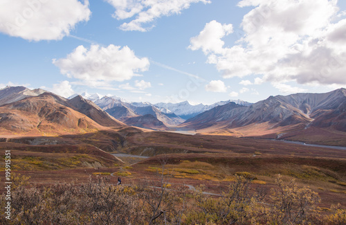Two walkers enjoying the fall color of a beautiful day in Denali National Park with the dramatic Central Alaskan Mountain Range in the background