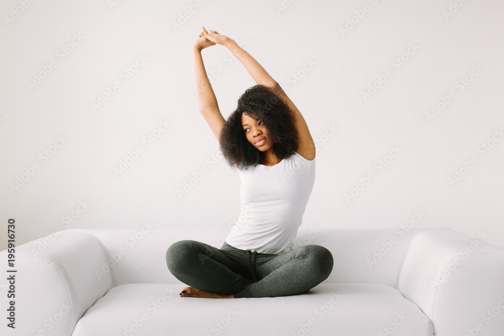 An African American young women sitting in the lotus position on white bed
