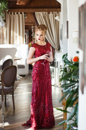 Beautiful woman posing in red long dress with train in luxury restaurant interior