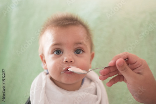 Blue eyed baby boy eating yogurt in the spoon