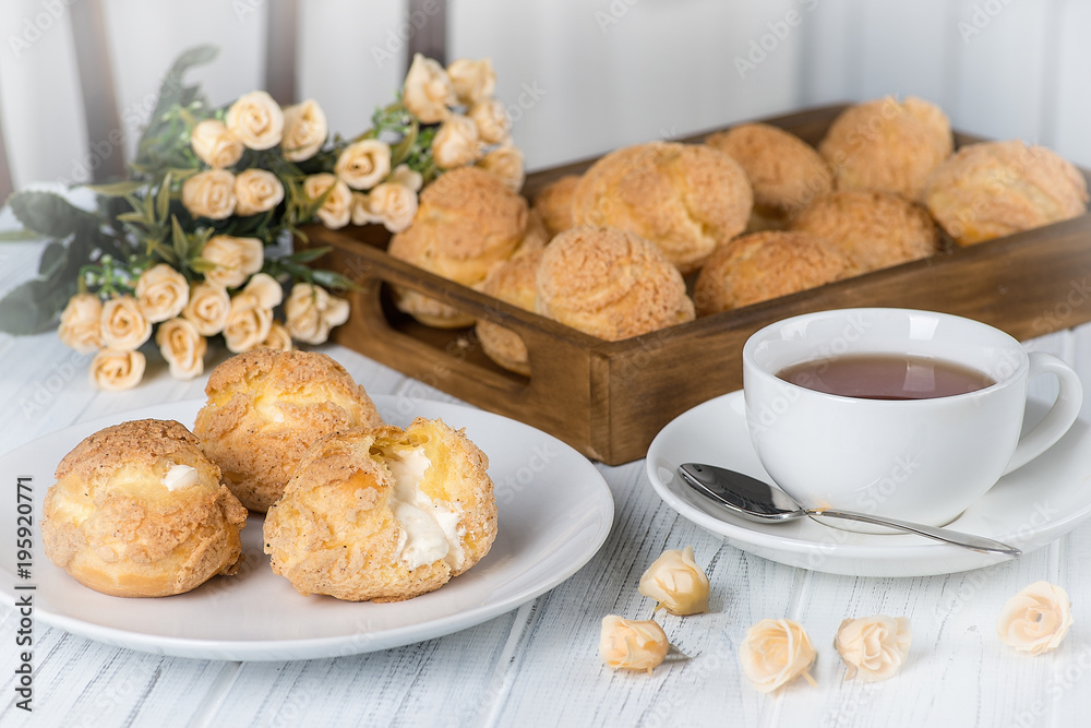 Many tasty cakes of Shue from custard paste with cream stuffing lie on a round plate on a white wooden table. Many tasty cakes of Shue from custard paste with cream stuffing lie on a round plate on a white wooden table.