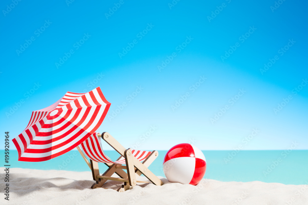 Lounge chair with parasol and beach ball on the coast