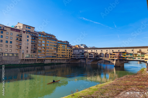 Arno river with unknown man on kayak, houses and old Ponte Vecchio bridge, Florence, Tuscany, Italy