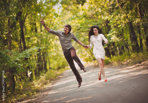 Fototapeta Naklejka Na Ścianę i Meble -  Young boy and girl are running along the road and jumping up fun. The newlyweds laugh happily. Hooray concept.