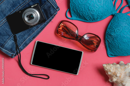Smartphone, Swimsuit, Jeans, Sunglasses, Photo Camera, Seashell on Pink Background. Top View Travel Concept Mock up.