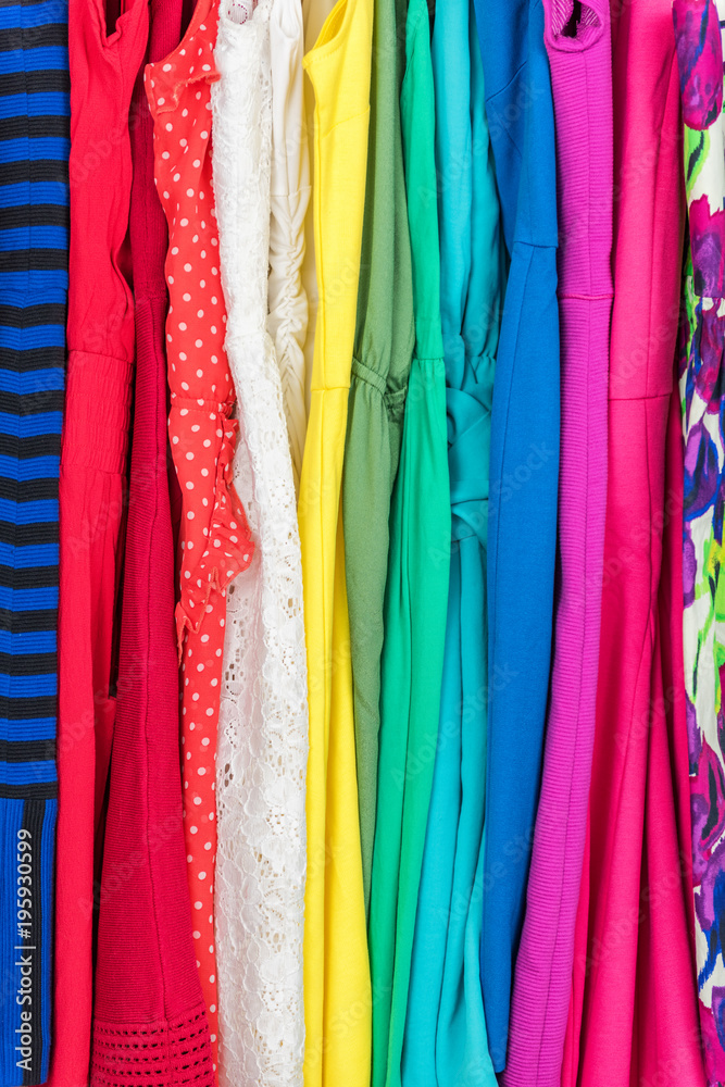 Clothing closet many colorful dresses, variety of fabric and patterns for summer fashion . Women's clothes selection closeup of texture in pink, red, green, blue dress, with stripes, lace, polka dots.