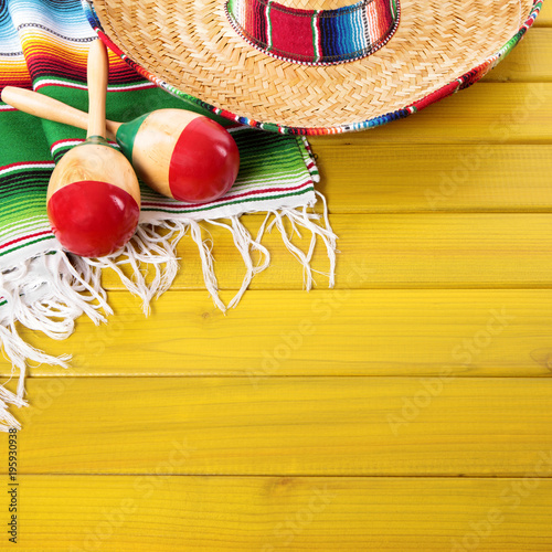 Mexico cinco de mayo background border square format with sombrero straw hat traditional rug or blanket and maracas on an old yellow pine wood background fiesta carnival photo