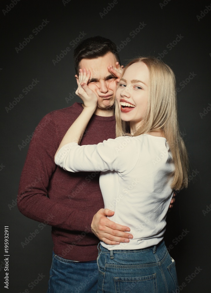 Portrait of a beautiful young couple in love posing at studio over dark background. The girl plays with the face of her boyfriend Portrait of a beautiful young couple in love posing at studio over dark background. The girl plays with the face of her boyfriend