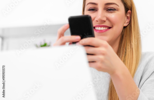 Attractive young woman with a smartphone in her hand at the office desk with a laptop.