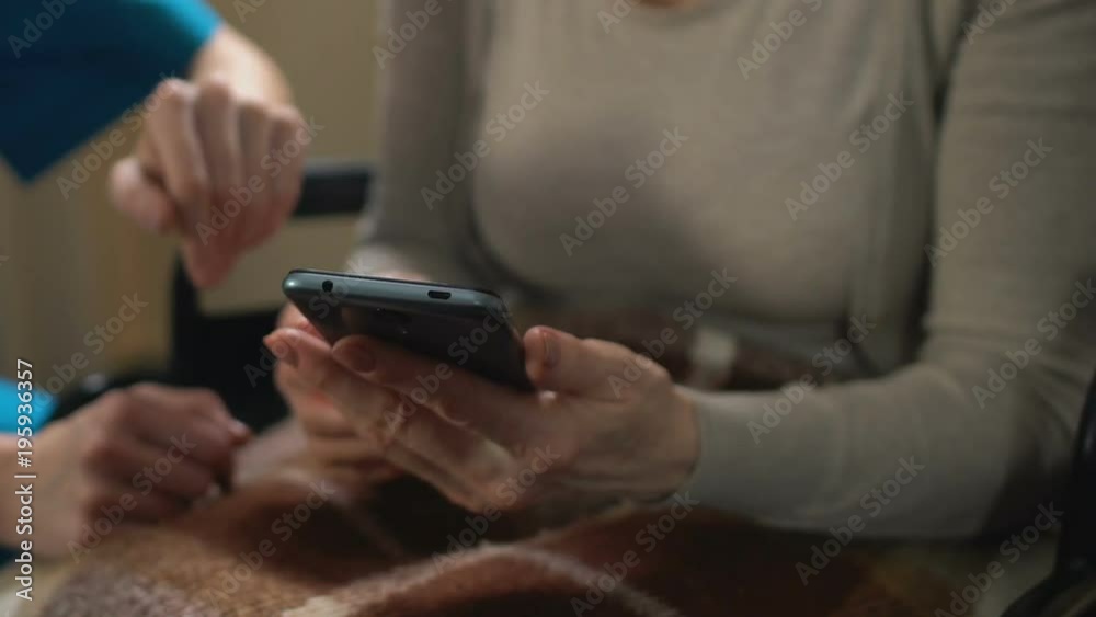 Nurse helping old woman with disabilities to shop online, using mobile app Nurse helping old woman with disabilities to shop online, using mobile app