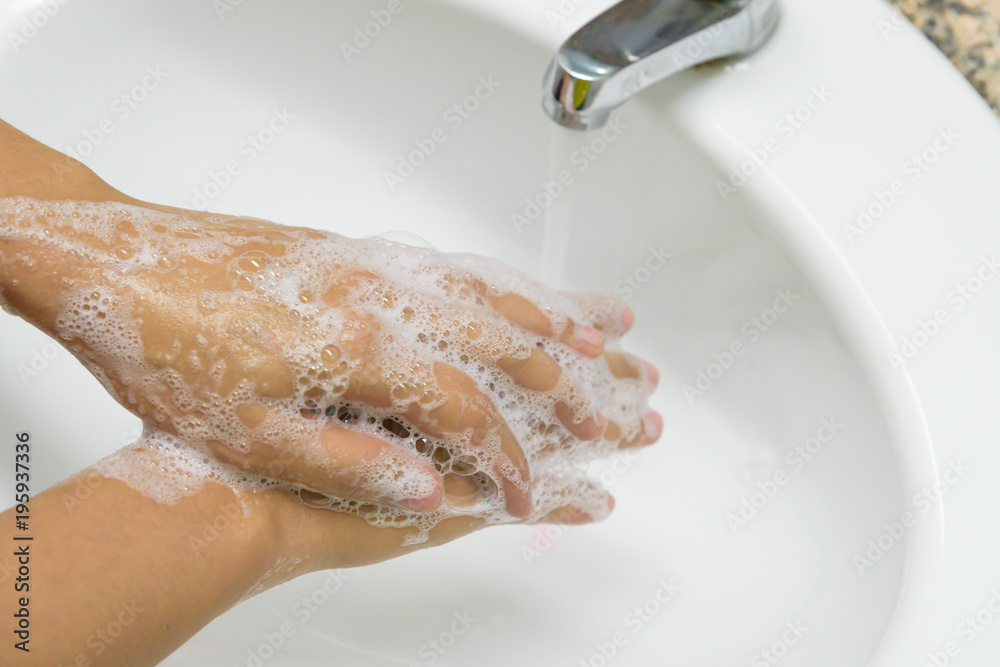 Fototapeta premium Woman washing hands with soap under the faucet with water in the bathroom.