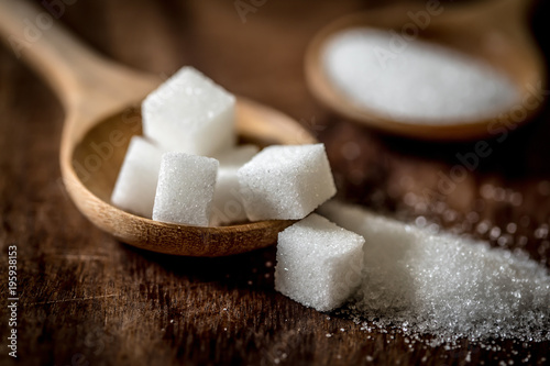 Photo Close up the sugar cubes and cane in wooden spoon on the table
