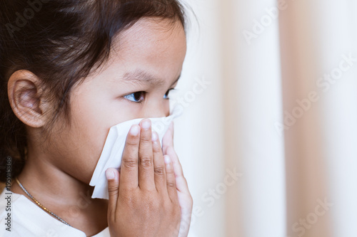 Sick asian little child girl wiping and cleaning nose with tissue on her hand in the hospital